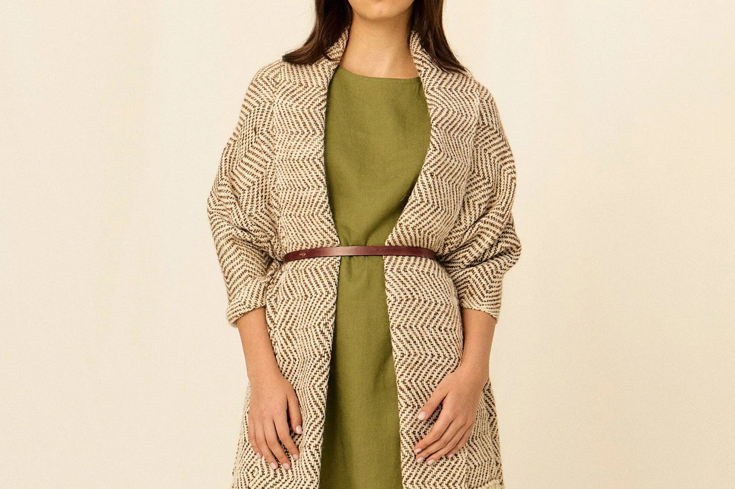 Woman wearing a long, patterned beige cardigan with tassels over a green dress on a beige background